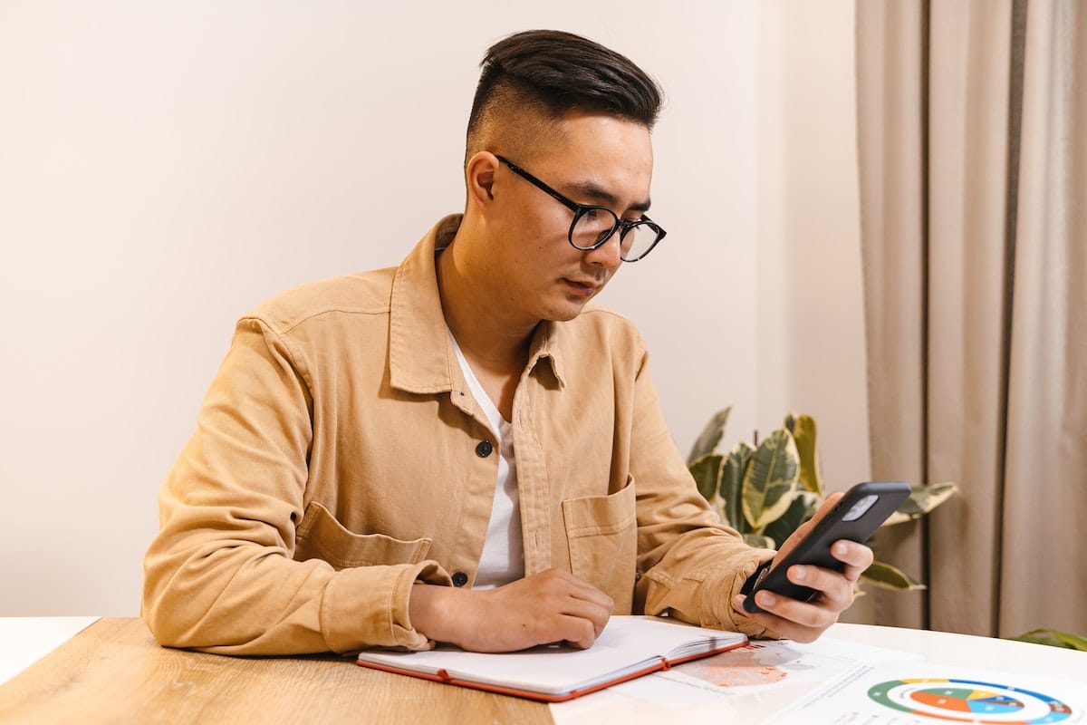 Man Sitting at a Table with a Smart Phone and Notebook